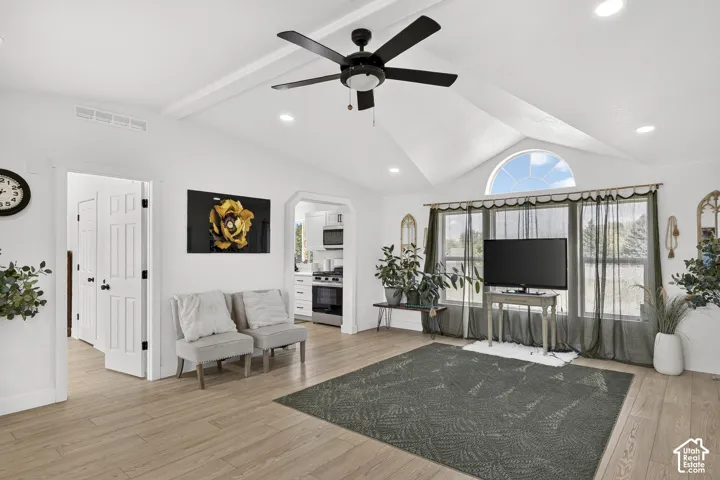 Vaulted ceiling with exposed beams, wood-finish flooring, a contemporary ceiling fan, recessed lighting, and a half-round window