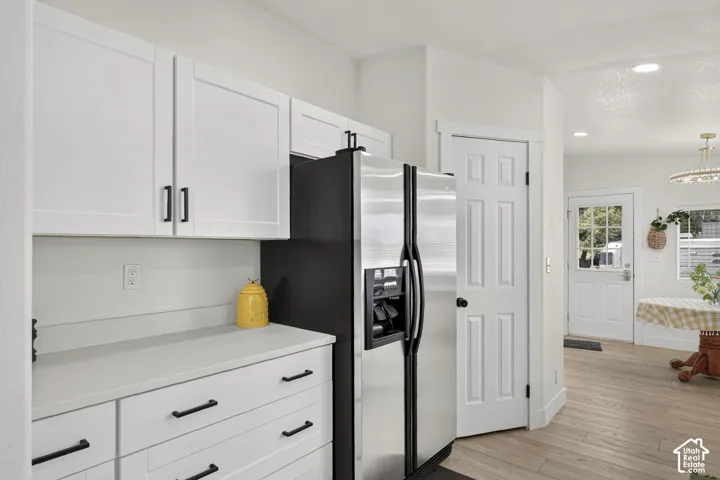White shaker cabinetry with black hardware, stainless steel refrigerator, light wood-finish flooring, and a paneled door