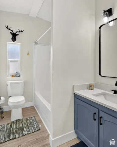 Full bathroom featuring a white bathtub and shower combination, a single-sink vanity with a blue cabinet, wood-finish flooring, and a window with privacy glass