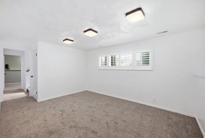 Textured white ceiling with flush-mount lighting, white walls, and a window featuring white plantation shutters