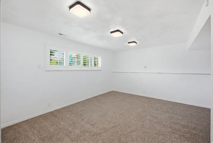 Recessed window with white plantation shutters, three flush-mount ceiling lights, and light-toned carpet flooring