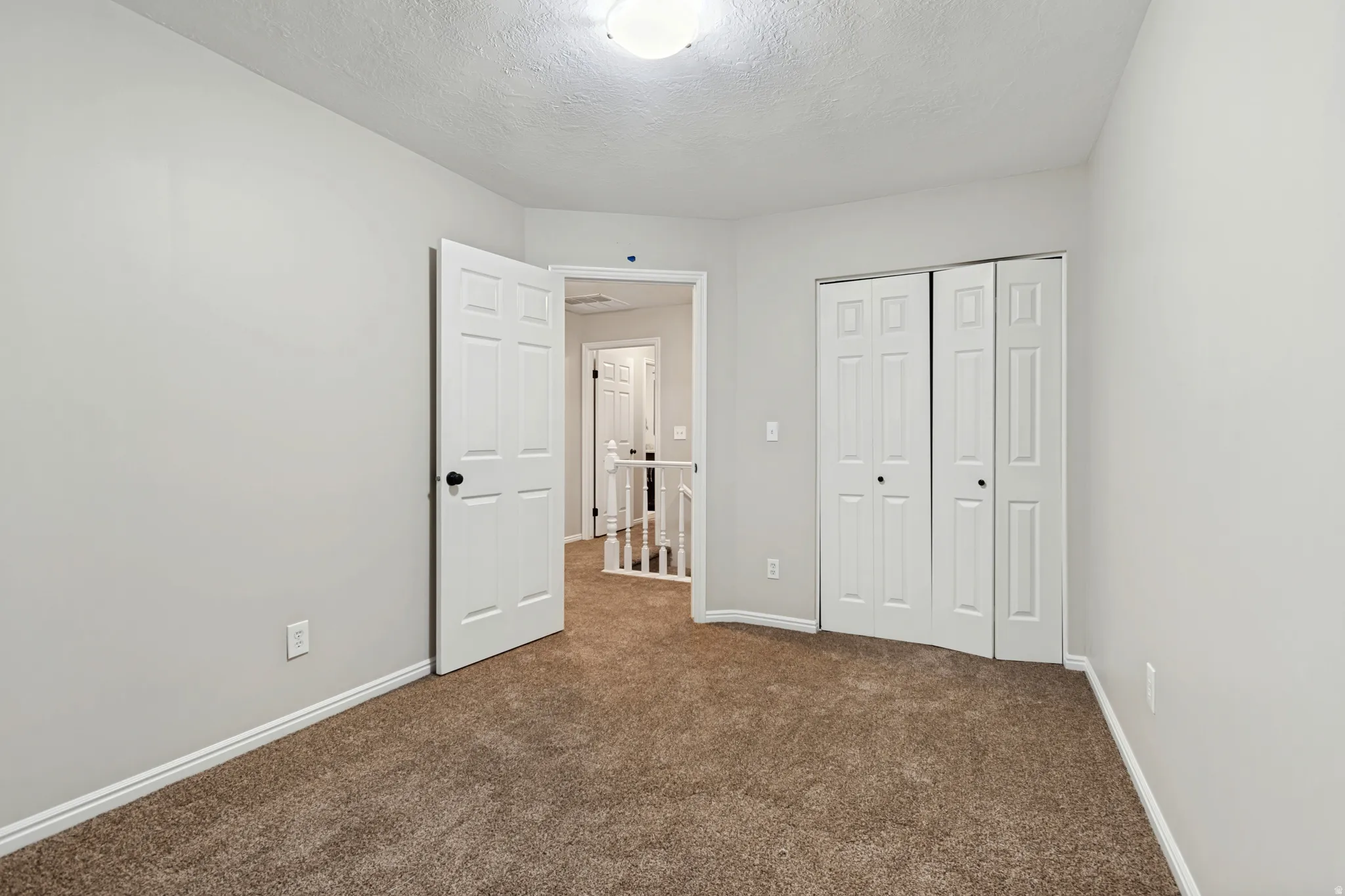 Plush carpeting, light neutral wall paint, ceiling-mounted light fixture, and white bi-fold closet doors