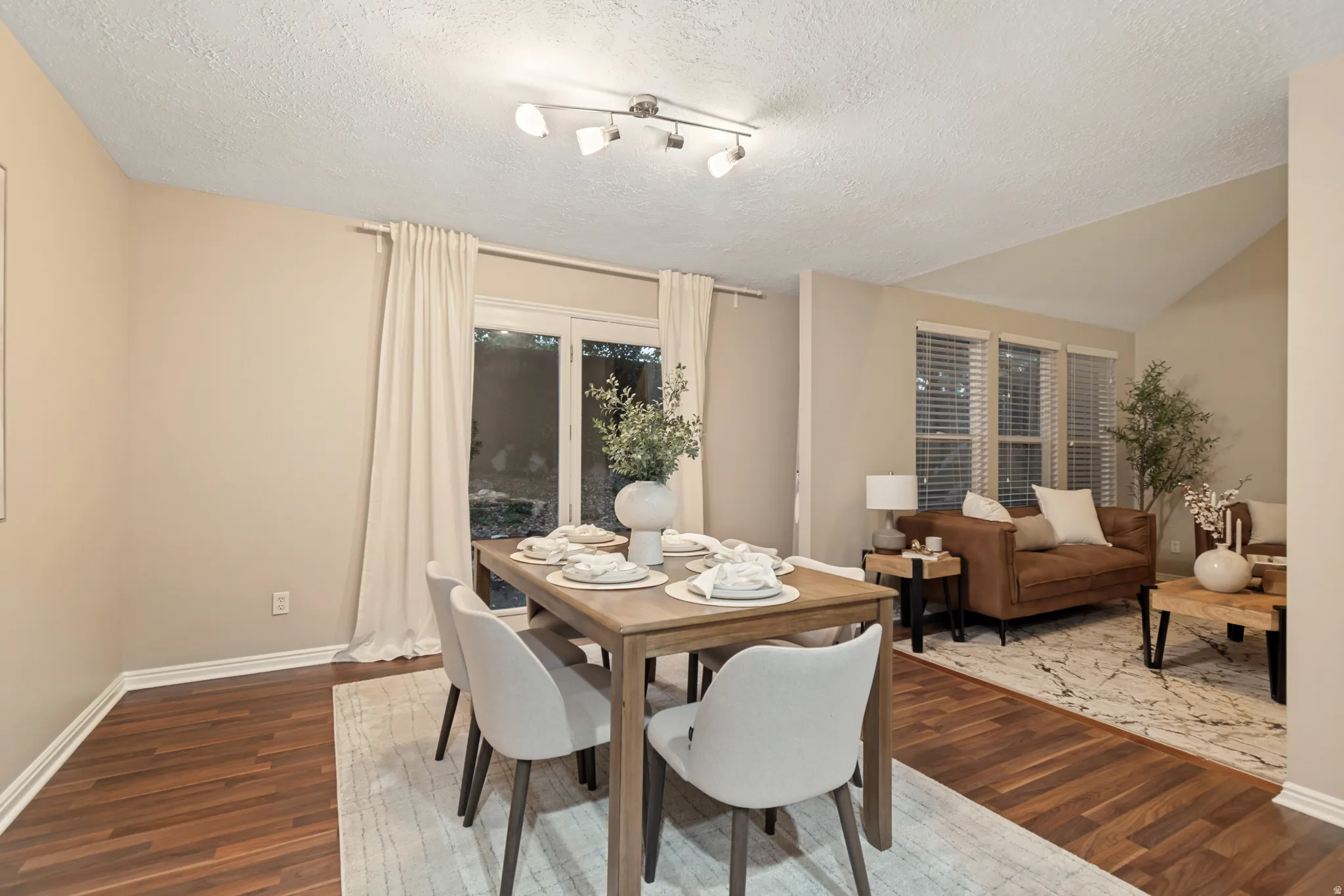 Wood-finish flooring, vaulted ceiling, track lighting, sliding glass doors, and window blinds