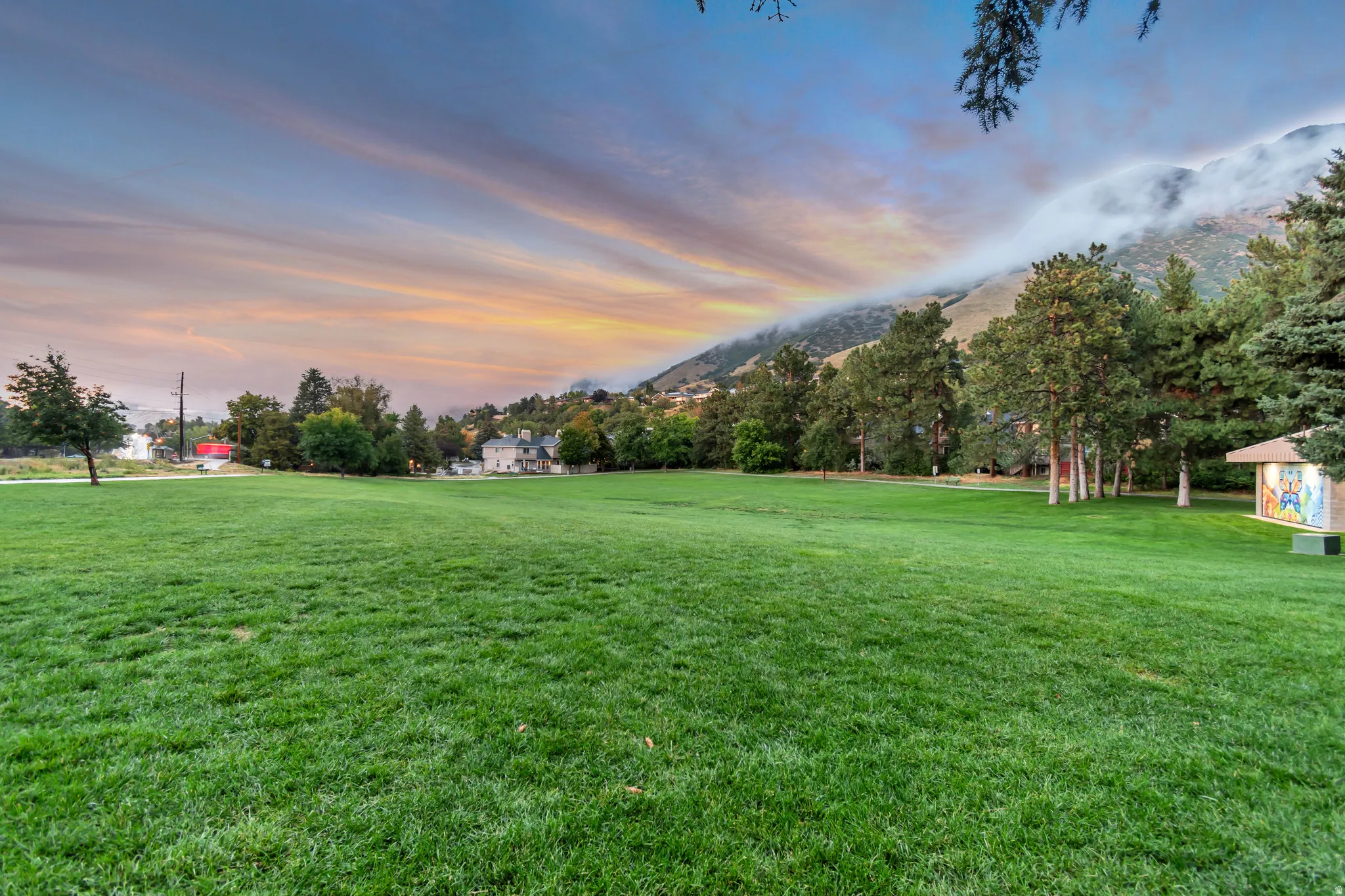 Expansive green space featuring a manicured lawn, mature trees, and distant mountain backdrop