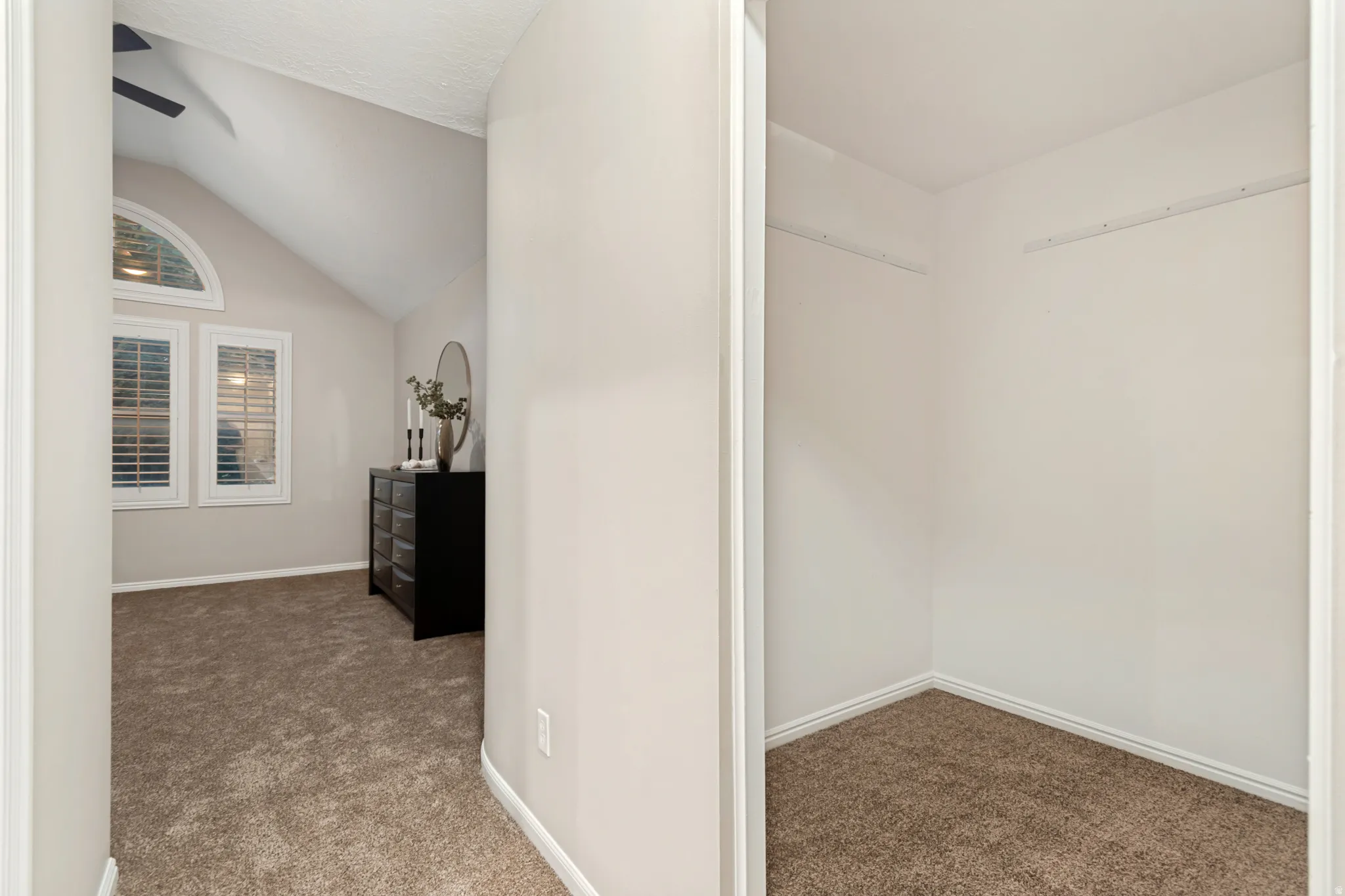 Vaulted ceiling, arched transom window, two rectangular windows with plantation shutters, ceiling fan, and carpet flooring