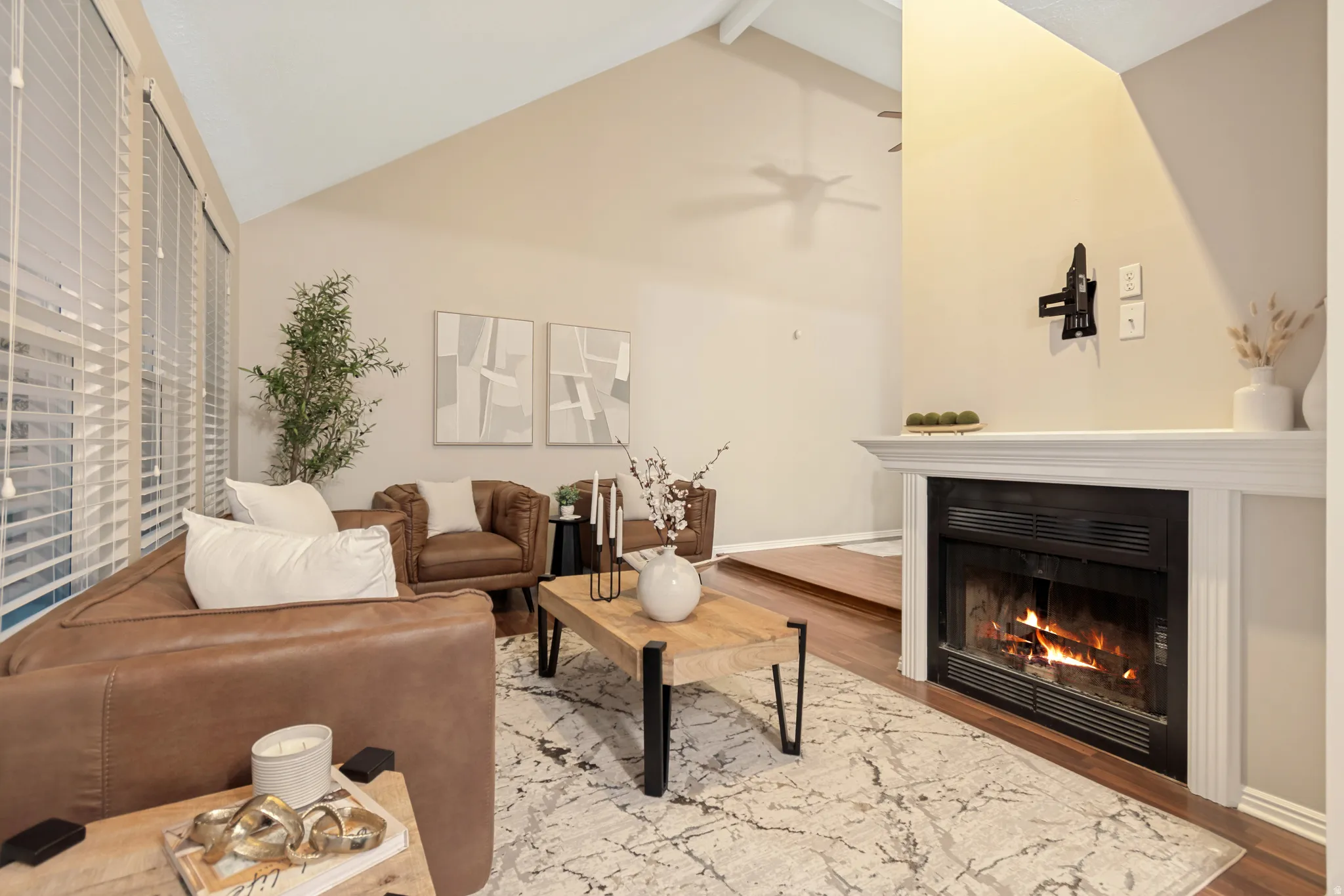 Vaulted ceiling, fireplace with white mantel, wood-finish flooring, and horizontal blinds