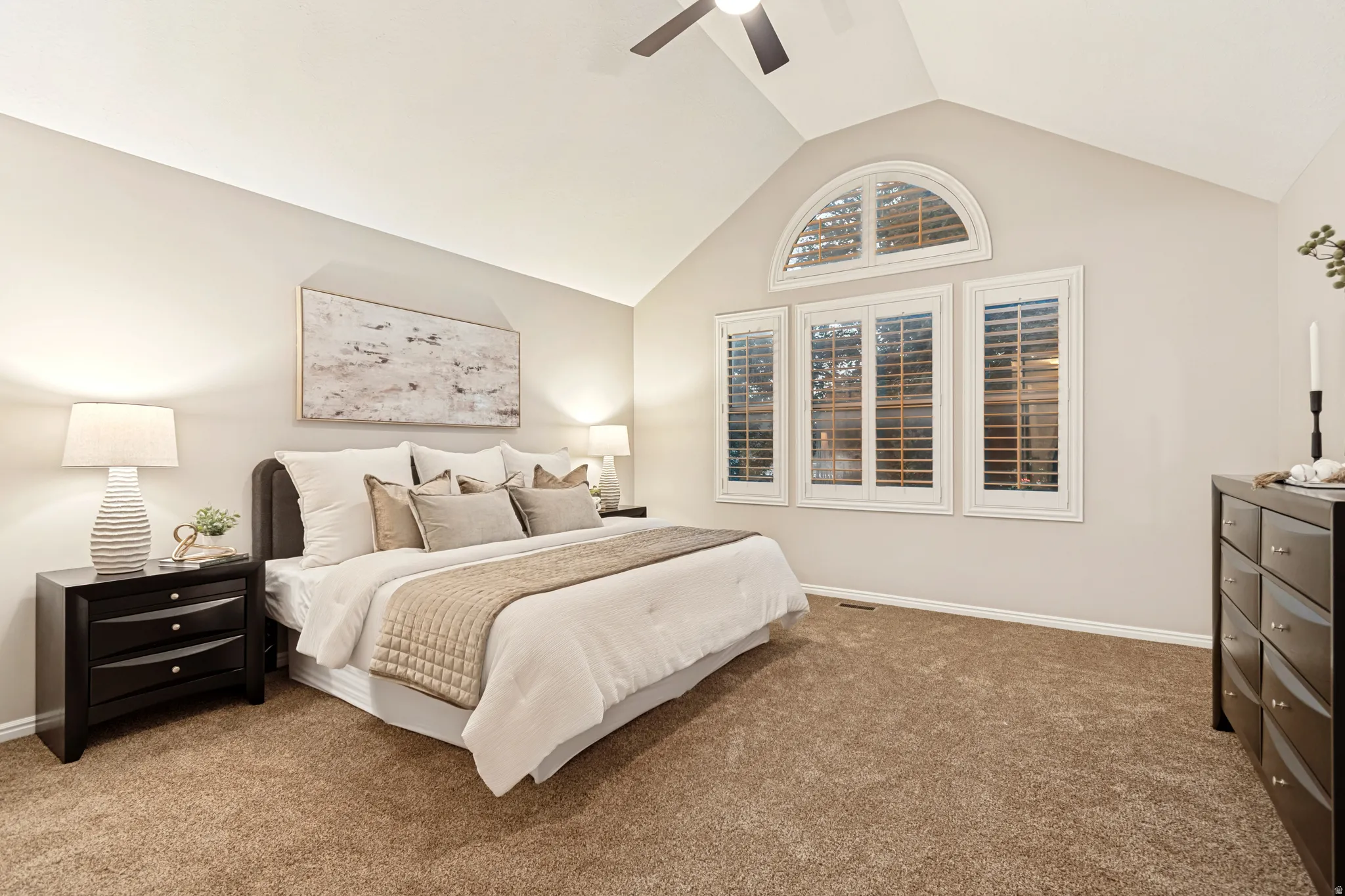 Vaulted ceiling with ceiling fan, arched transom window, plantation shutters, and soft-tone carpeting