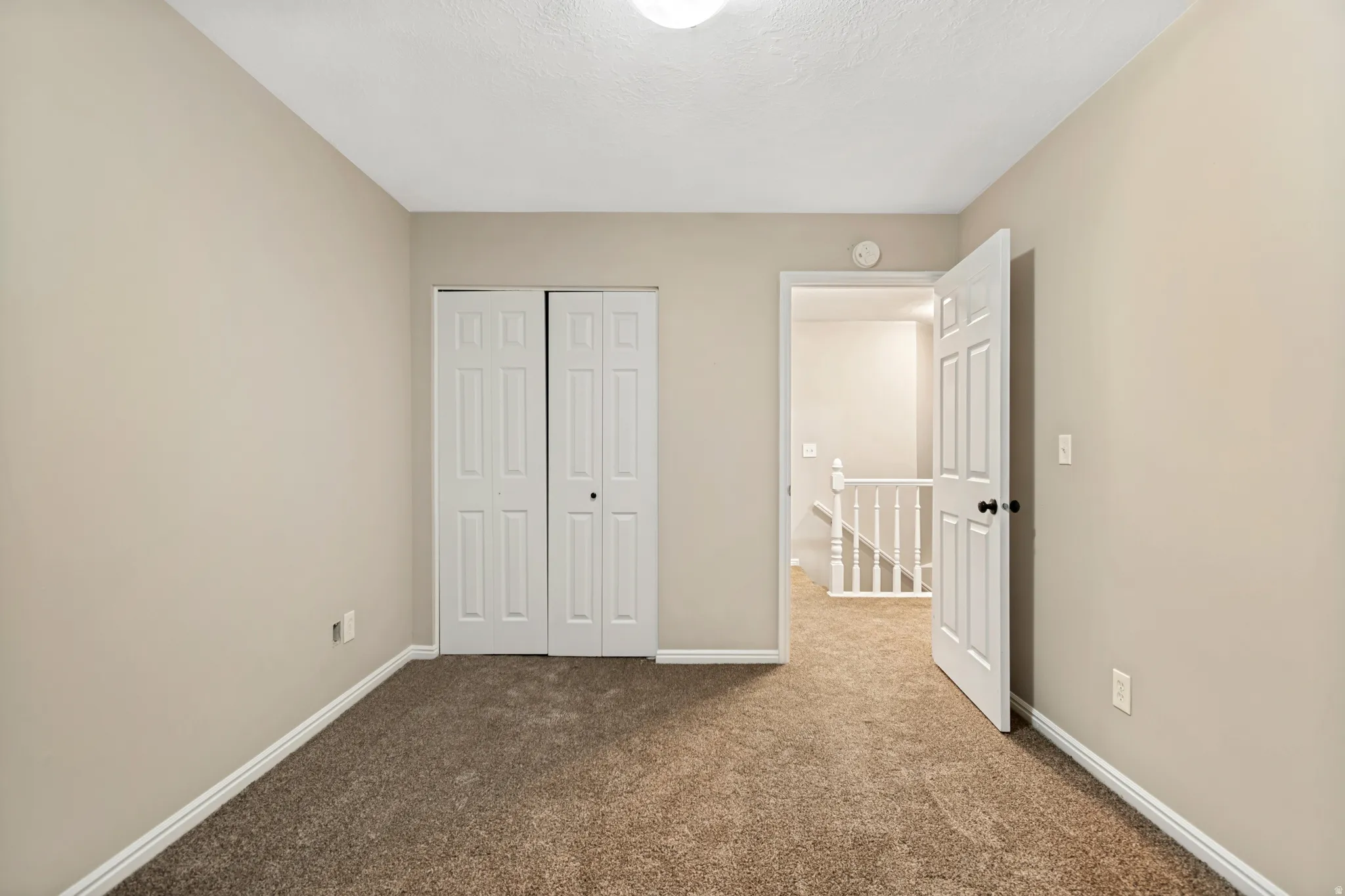 Neutral-toned walls, carpeted flooring, white trim, bi-fold closet doors, and a paneled interior door