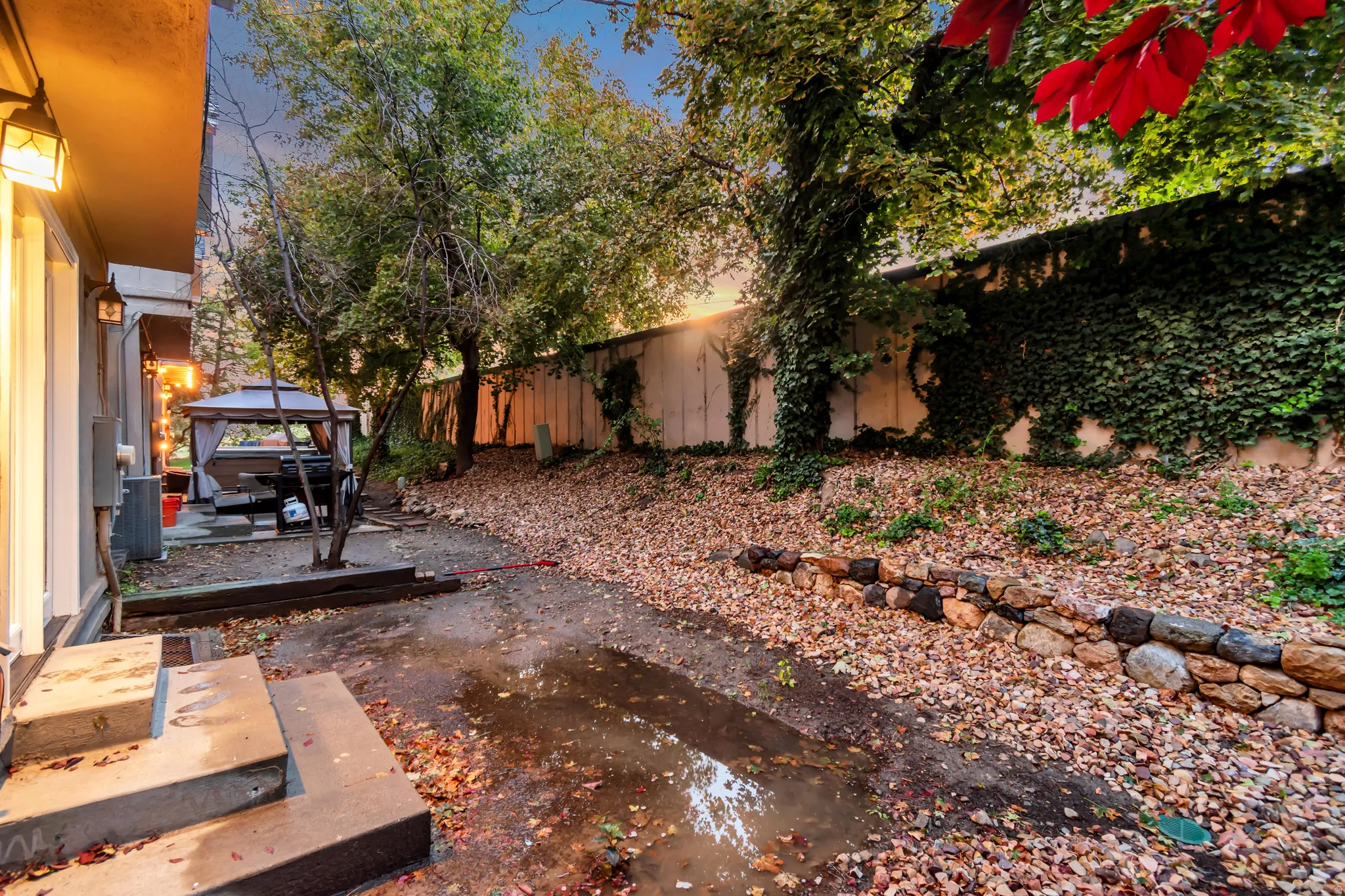 Tiered backyard featuring a stone retaining wall, mature trees, and an ivy-covered privacy fence