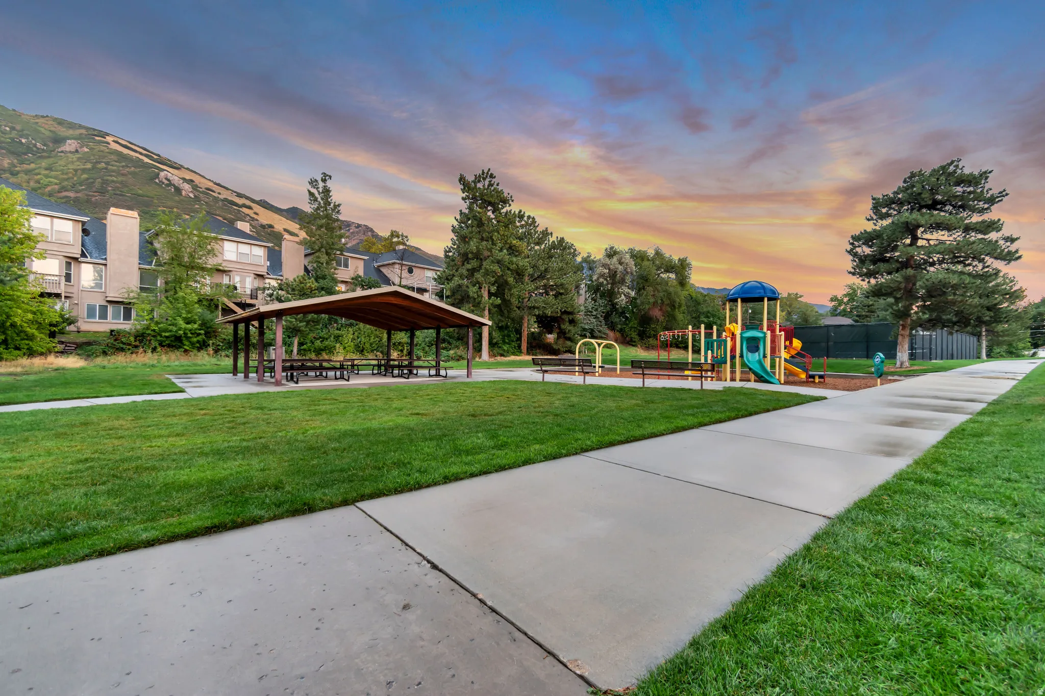 Expansive grassy area with a paved pathway, covered picnic structure, and a vibrant playground