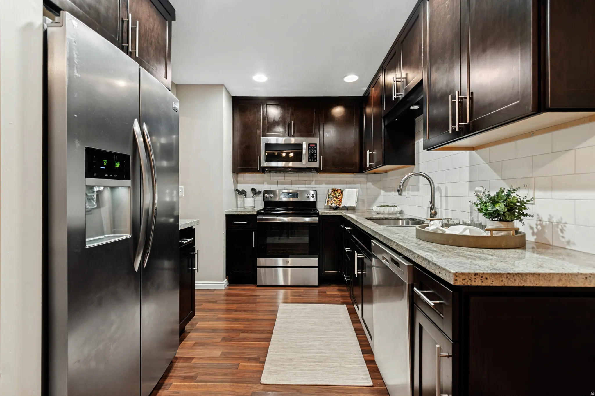 Gourmet kitchen featuring wood-finish flooring, stainless steel appliances, dark wood cabinetry, white subway tile backsplash, and light-toned countertops