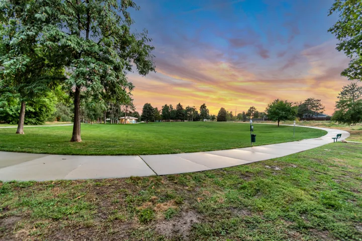 Expansive green space featuring a paved walking path, mature trees, and a distant building structure
