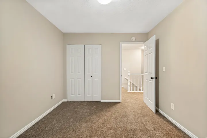 Neutral-toned walls, carpeted flooring, white trim, bi-fold closet doors, and a paneled interior door