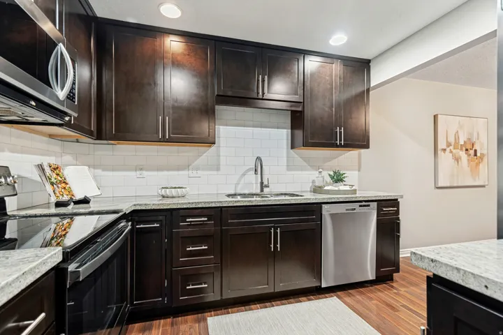 Kitchen featuring dark wood cabinetry, light-toned countertops, a white subway tile backsplash, stainless steel appliances, and wood-finish flooring