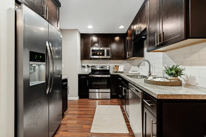 Gourmet kitchen featuring wood-finish flooring, stainless steel appliances, dark wood cabinetry, white subway tile backsplash, and light-toned countertops