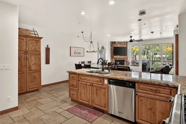Kitchen island with stone countertop, integrated sink, stainless steel dishwasher, and wood cabinetry