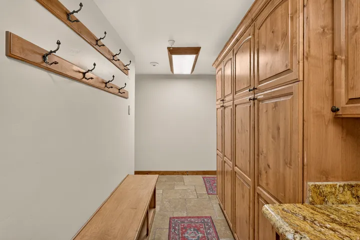 Built-in wood cabinetry, natural stone tile flooring, wood-finish wall hooks, and a wood bench