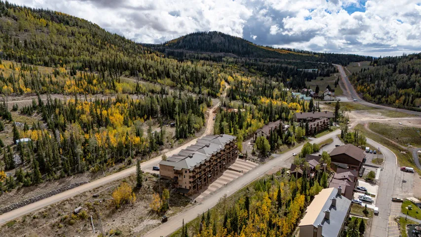 Multi-story building with multiple balconies, surrounded by mature trees and mountainous terrain