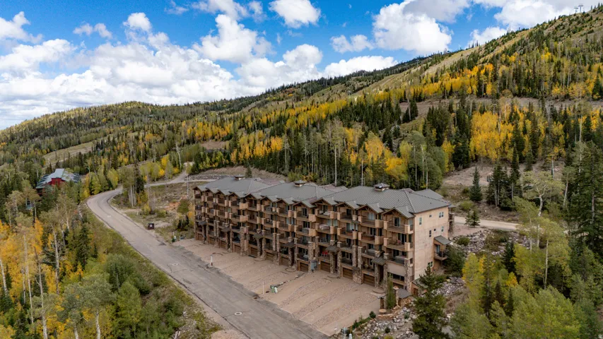 Multi-story residential building with private balconies and attached garages, set against a mountainous backdrop with abundant trees
