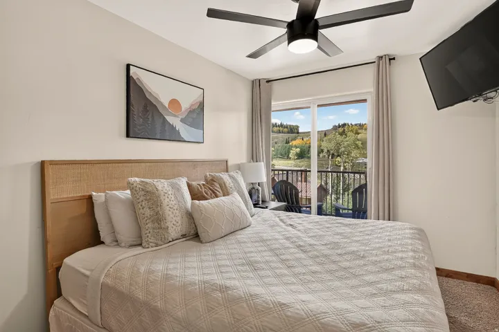 Sliding glass door leading to a balcony, black ceiling fan, wall-mounted television, and wood-finish trim