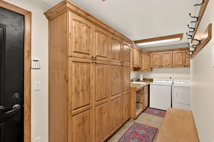 Laundry area featuring extensive wood-finish cabinetry, a built-in sink with countertop, and stone-finish flooring