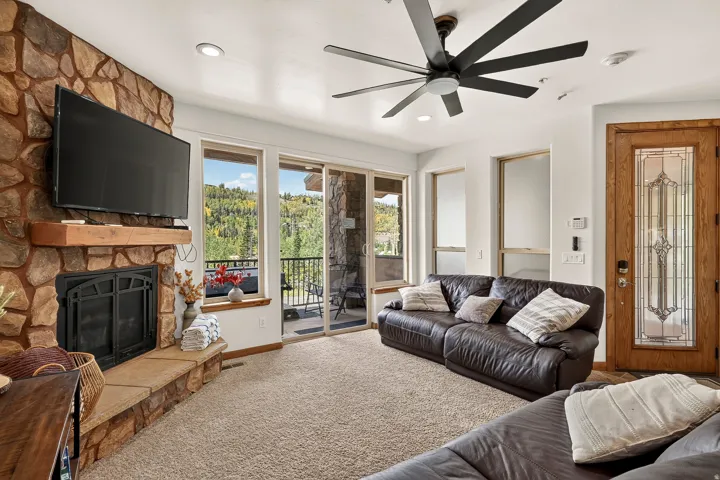 Stone-clad fireplace with a wood mantle, sliding glass door to exterior, recessed lighting, ceiling fan, and decorative front entry door