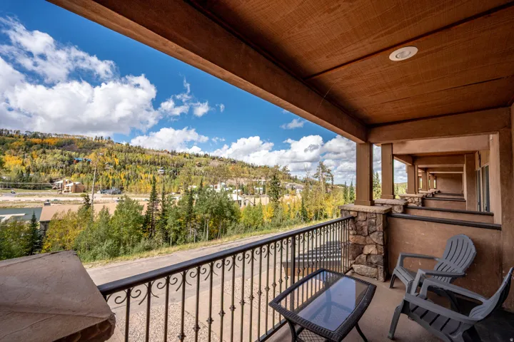 Covered balcony with a decorative wrought iron railing, stone column accents, and a textured ceiling with recessed lighting