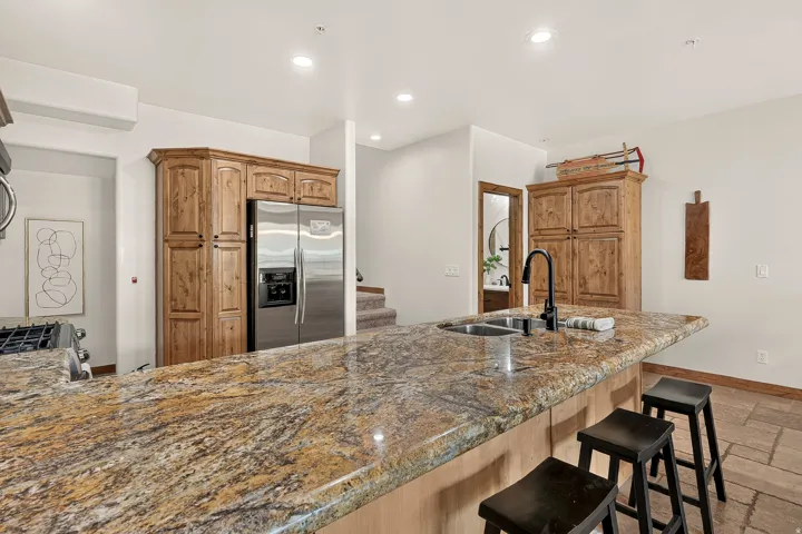 Kitchen island with a built-in sink and a matte black faucet, featuring a patterned stone countertop and wood-finish cabinetry