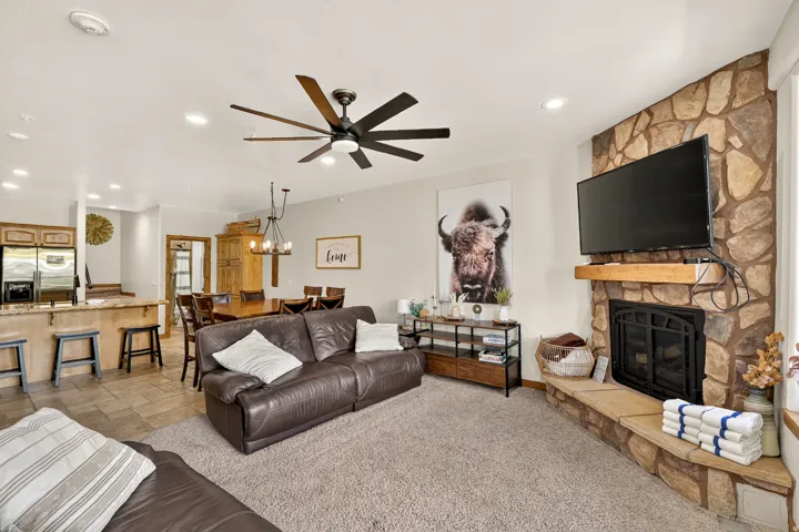 Stone-surround fireplace with a wood mantle, ceiling fan, recessed lighting, and tile flooring in the dining area