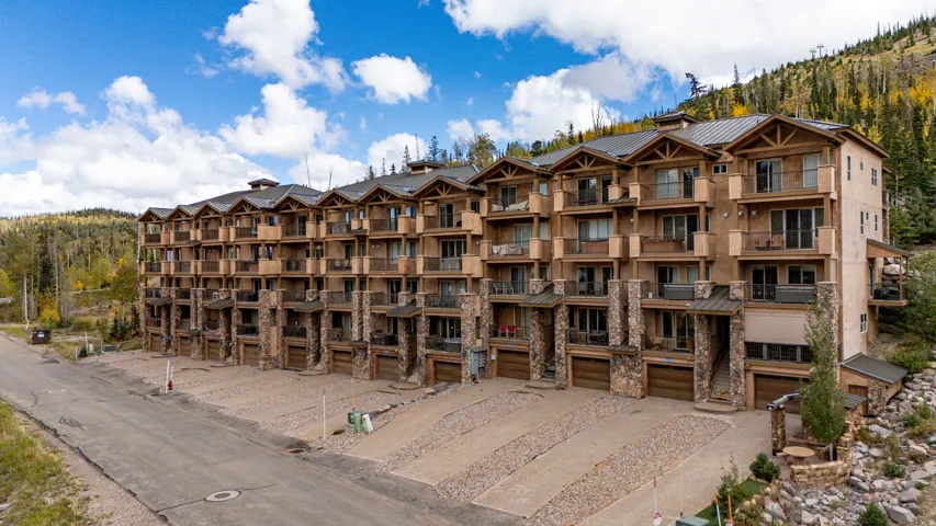 Multi-level residential building featuring stone and stucco exterior, individual garages, private balconies, and a sloped roofline