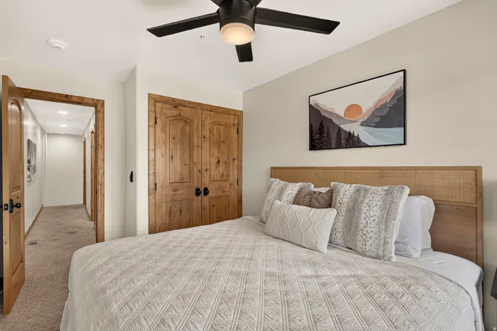 Carpeted flooring, a ceiling fan with integrated lighting, and a wood-paneled closet with dark hardware