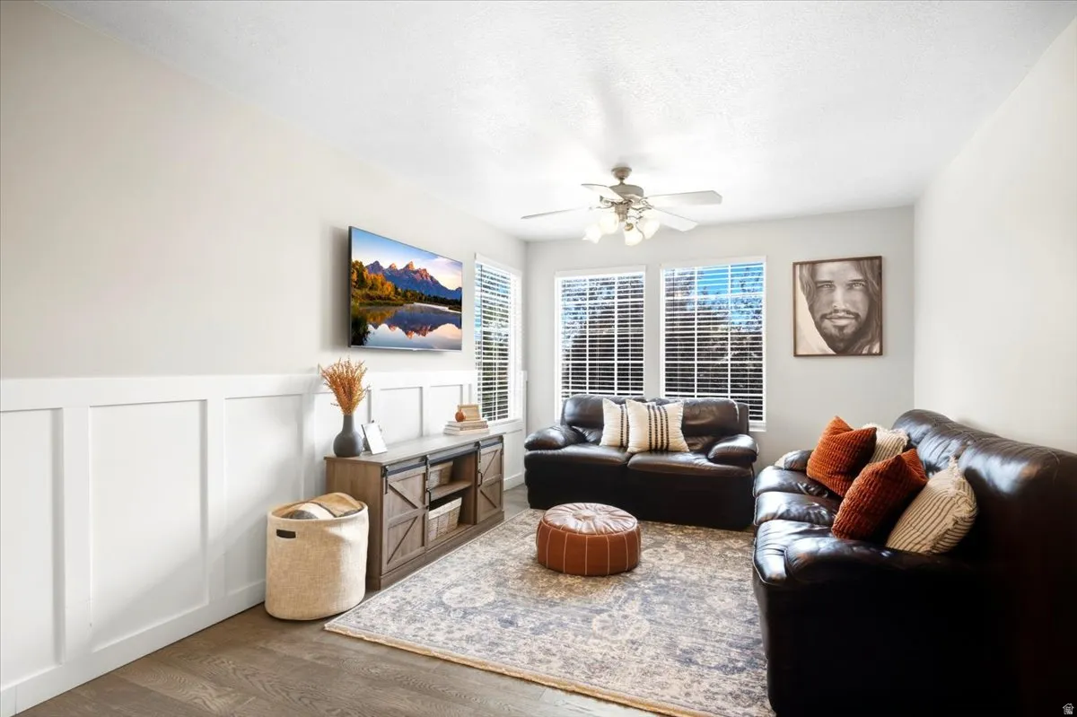 Wood-finish flooring, white paneled wainscoting, and a ceiling fan with integrated lighting