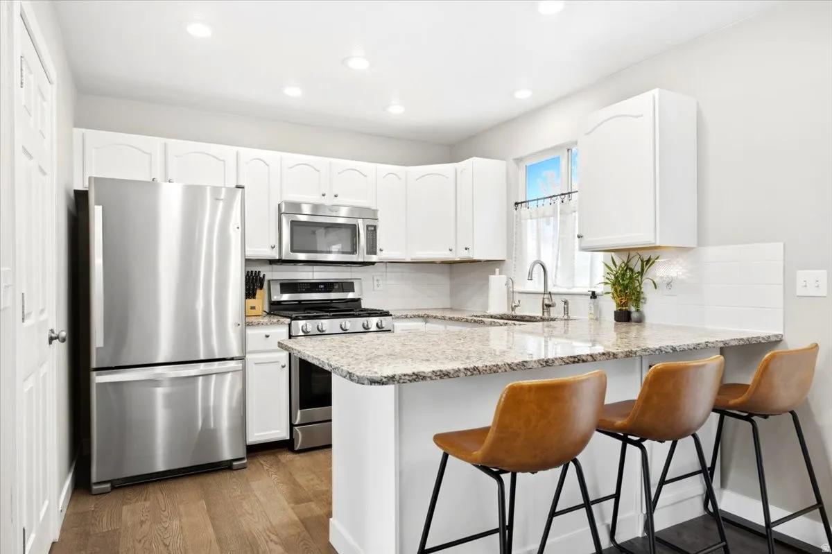 Modern kitchen featuring stainless steel appliances, white cabinetry, recessed lighting, wood-finish flooring, and a window above the sink