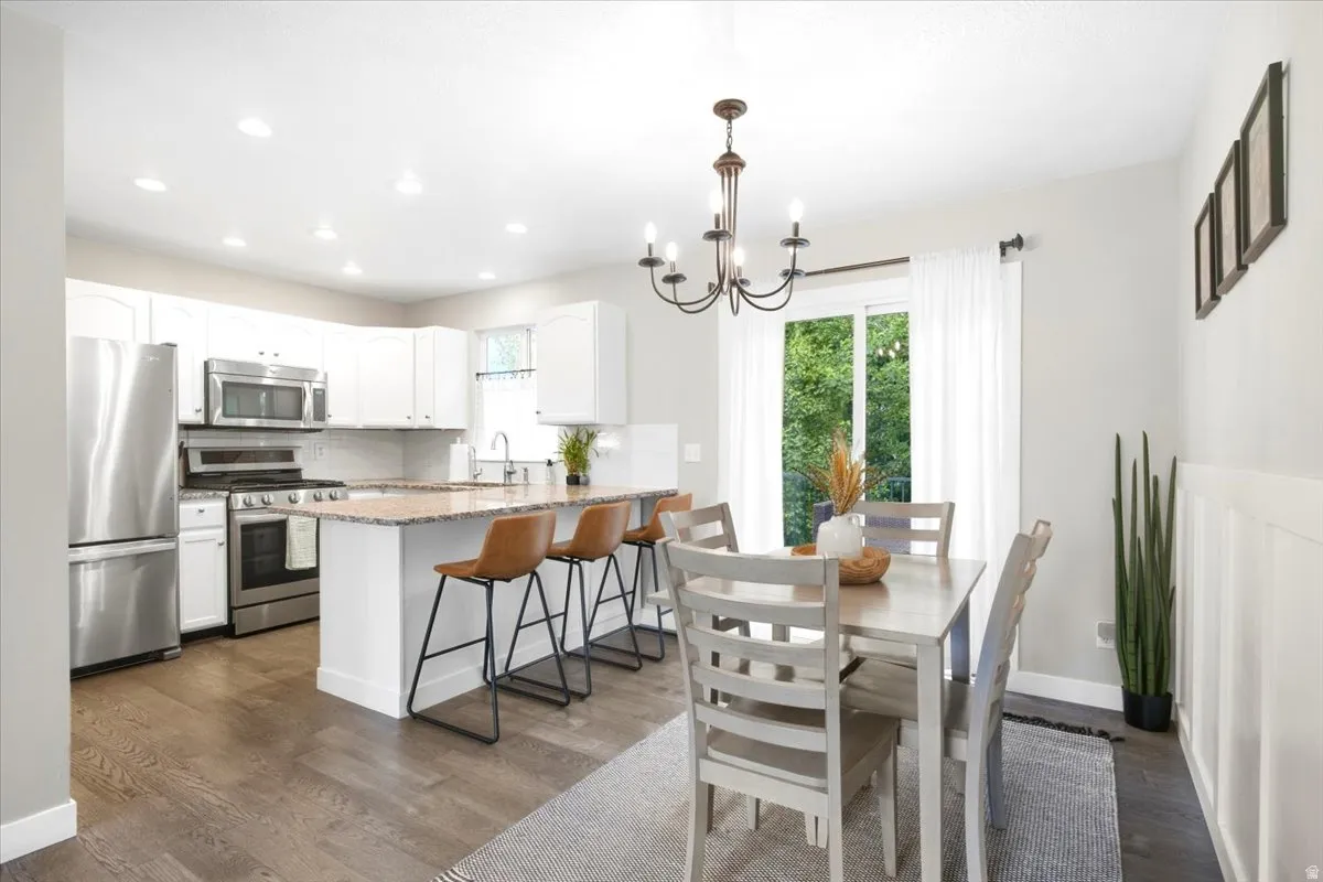 Open-concept kitchen and dining area featuring stainless steel appliances, white cabinetry, a kitchen island with seating, and wood-finish flooring