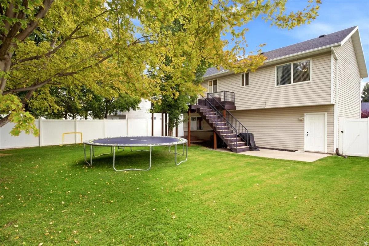 Expansive green lawn, mature trees, white privacy fencing, exterior staircase with dark handrails, and a ground-level access door