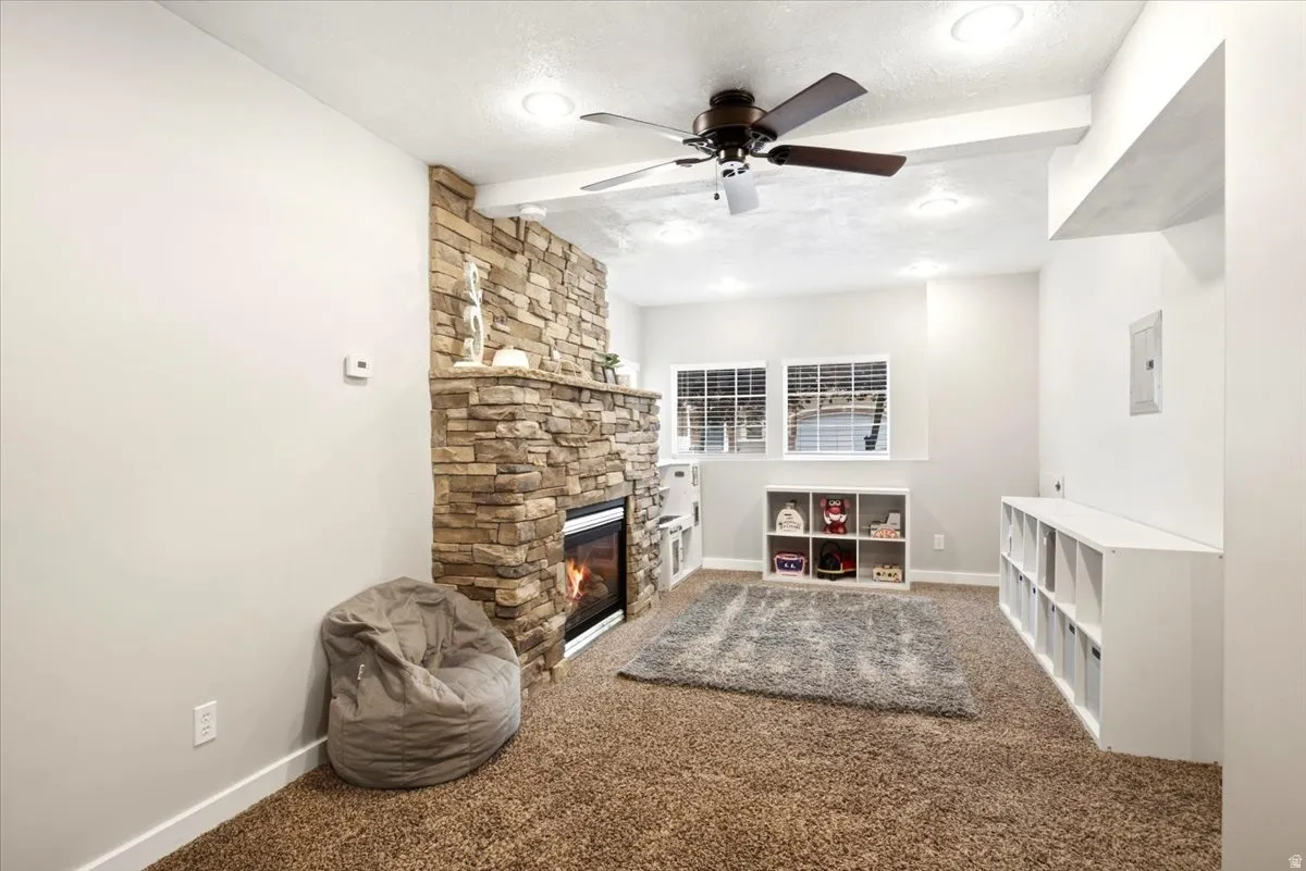 Stone-clad fireplace with a built-in electric insert, textured brown carpeting, recessed lighting, and a ceiling fan