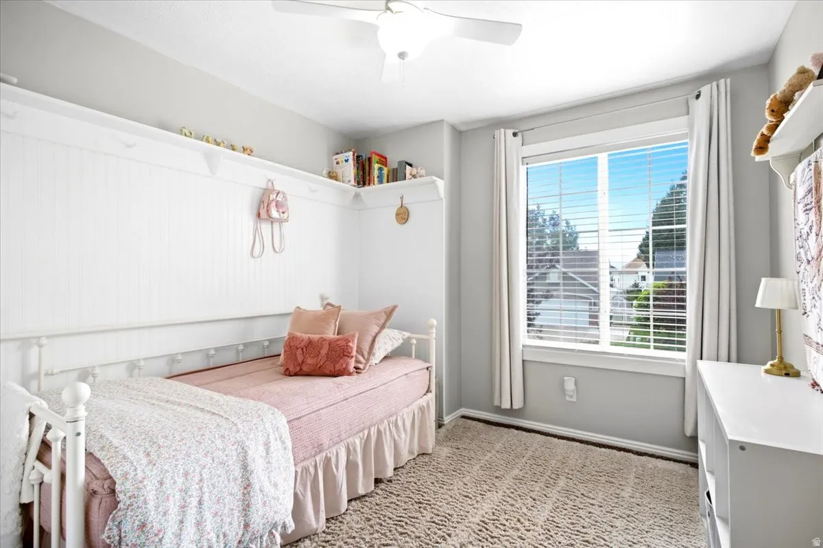Neutral painted walls, textured carpet flooring, white window treatments, and a ceiling fan with integrated lighting