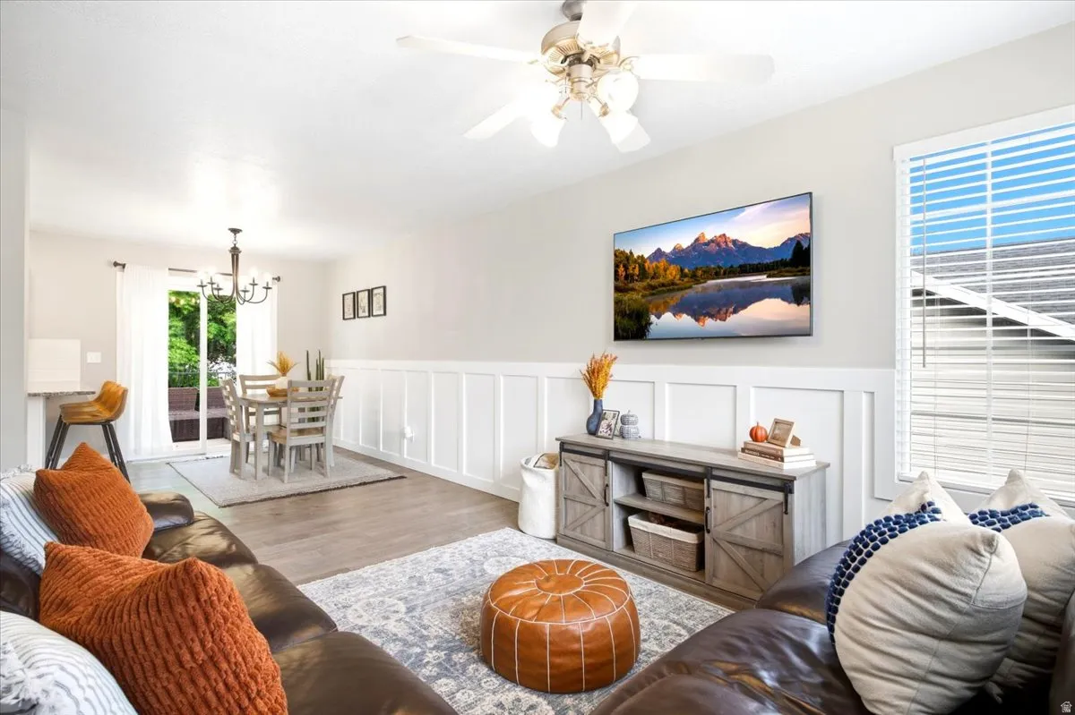 Light wood-finish flooring, white wall paneling, ceiling fan, sliding glass door, and a built-in breakfast bar