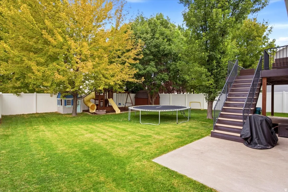 Expansive backyard featuring a manicured lawn, mature trees, a privacy fence, and a multi-level deck with stairs