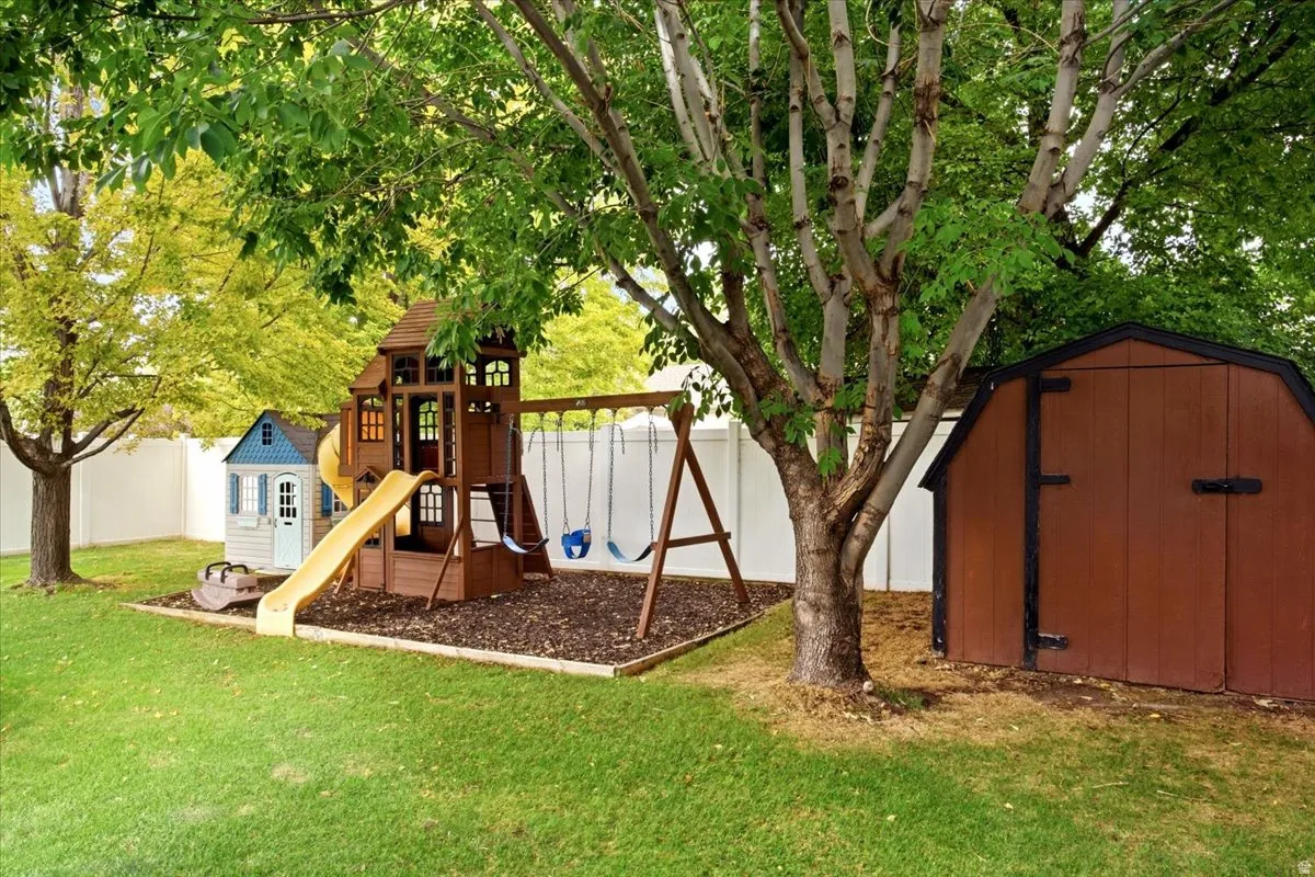 Expansive backyard featuring a wood play structure, a separate playhouse, and a brown storage shed