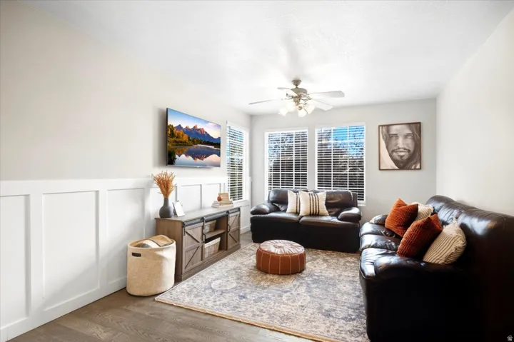 Wood-finish flooring, white paneled wainscoting, and a ceiling fan with integrated lighting