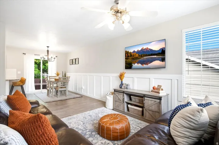 Light wood-finish flooring, white wall paneling, ceiling fan, sliding glass door, and a built-in breakfast bar