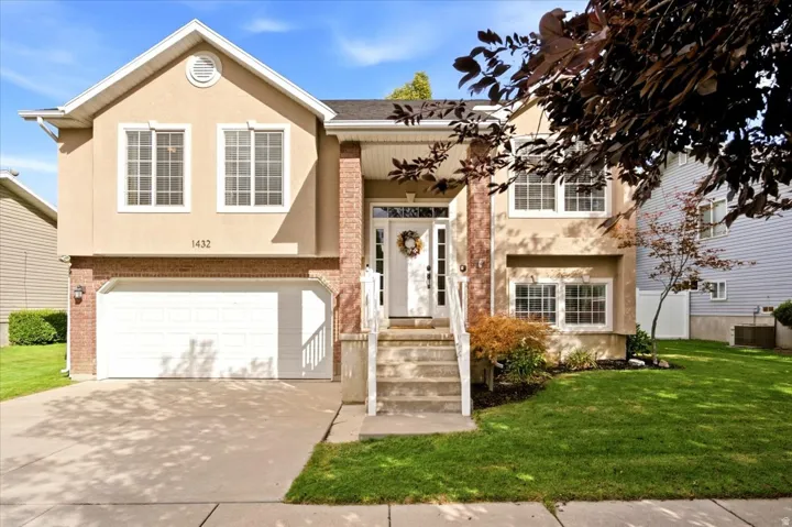 Stucco exterior with brick accents, attached two-car garage, concrete driveway, front porch with columns, and mature landscaping