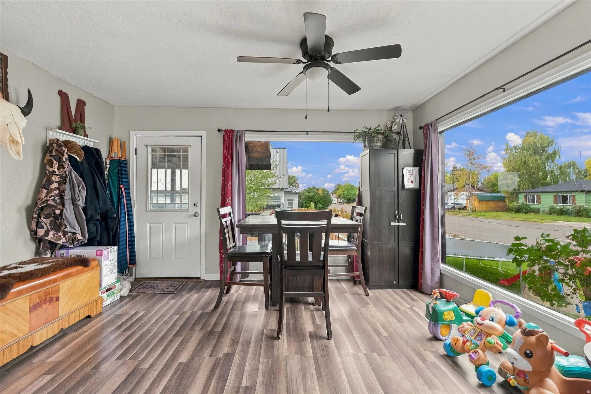 Wood-finish flooring throughout, ceiling fan with integrated lighting, white paneled door with window, and expansive window offering abundant natural light