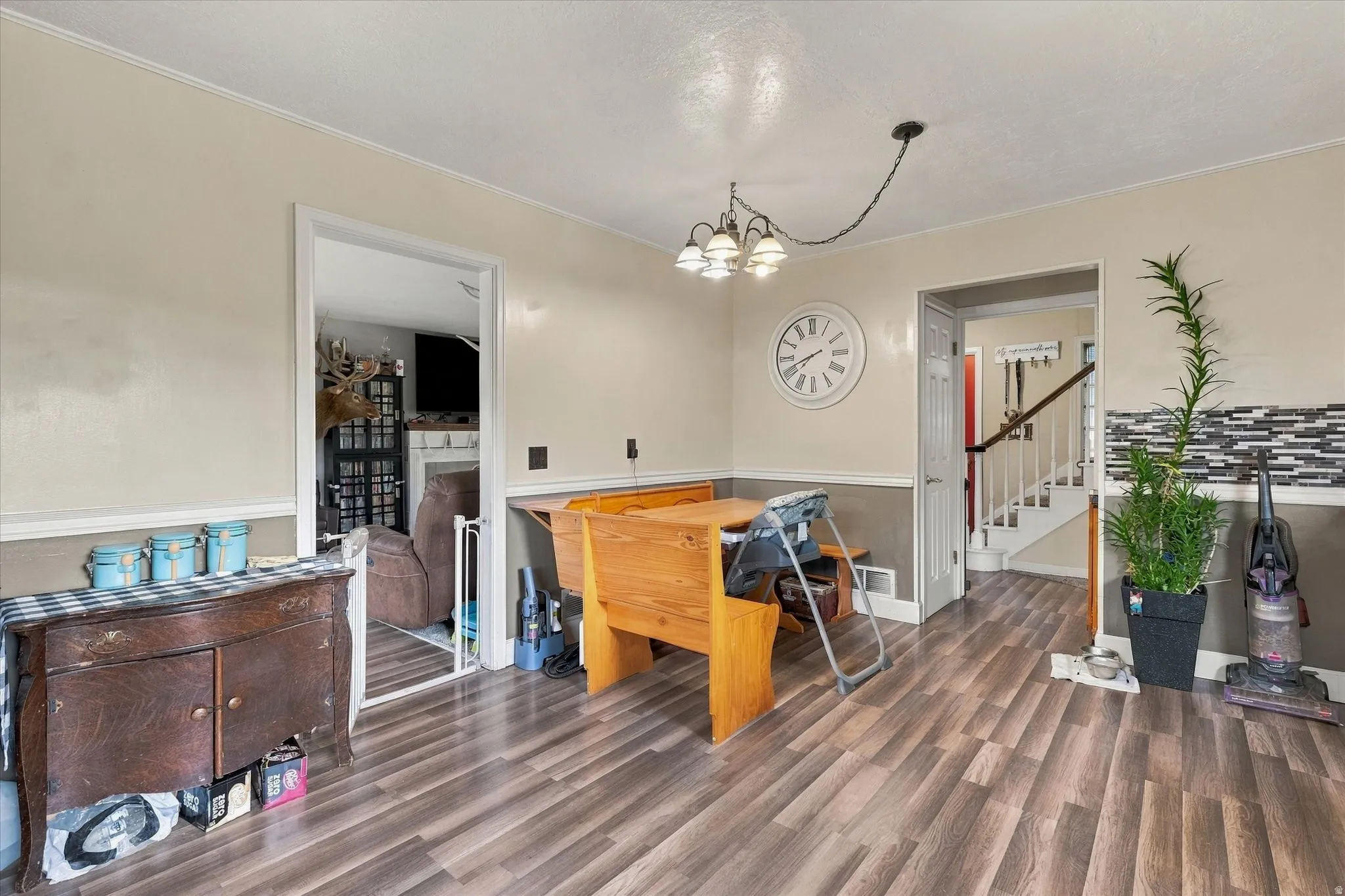 Wood-finish flooring, accent wall with decorative tile, chair rail molding, and a staircase with white risers and dark handrail