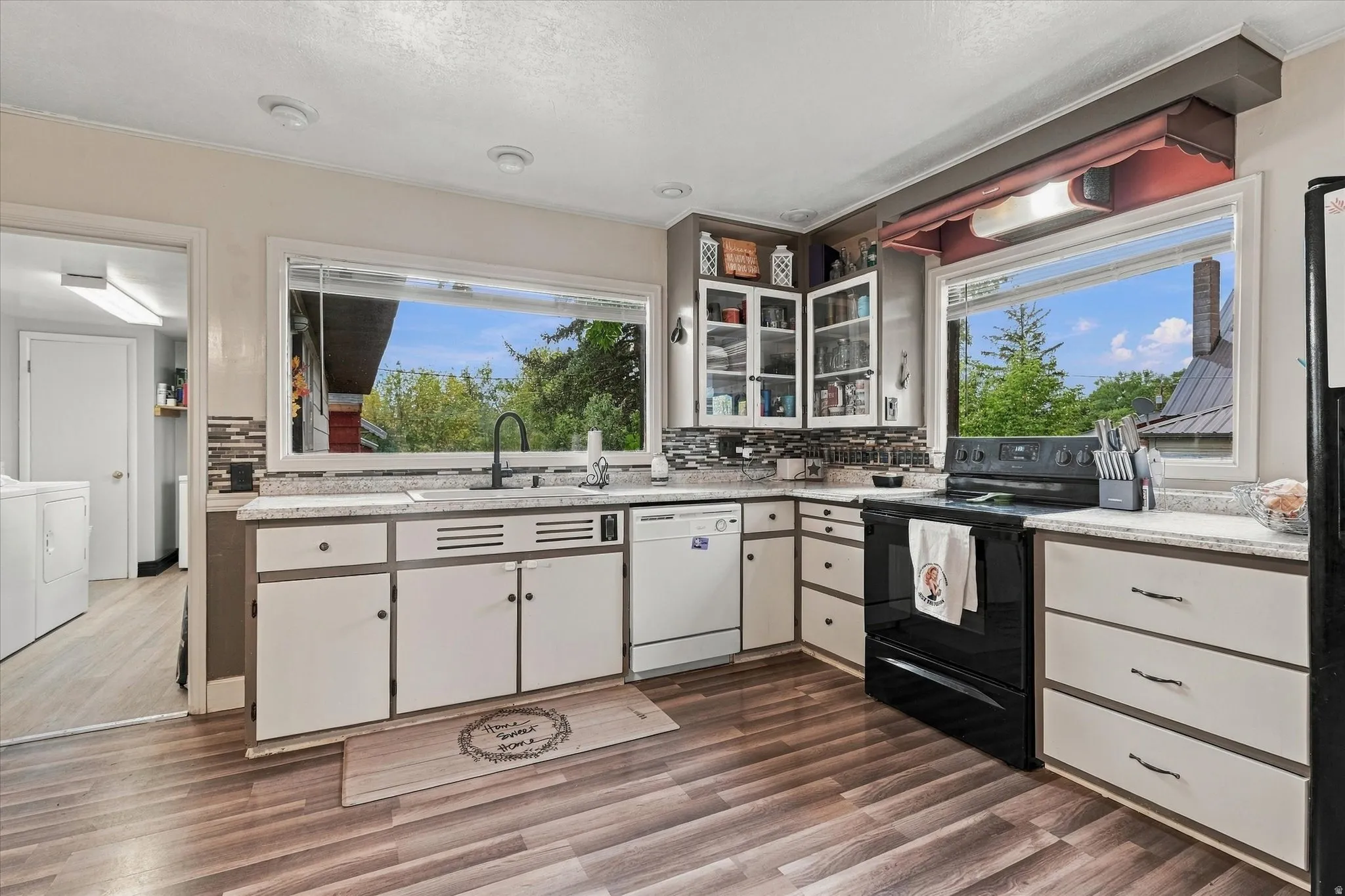 Wood-finish flooring with white cabinetry, stainless steel sink, and black stove appliance