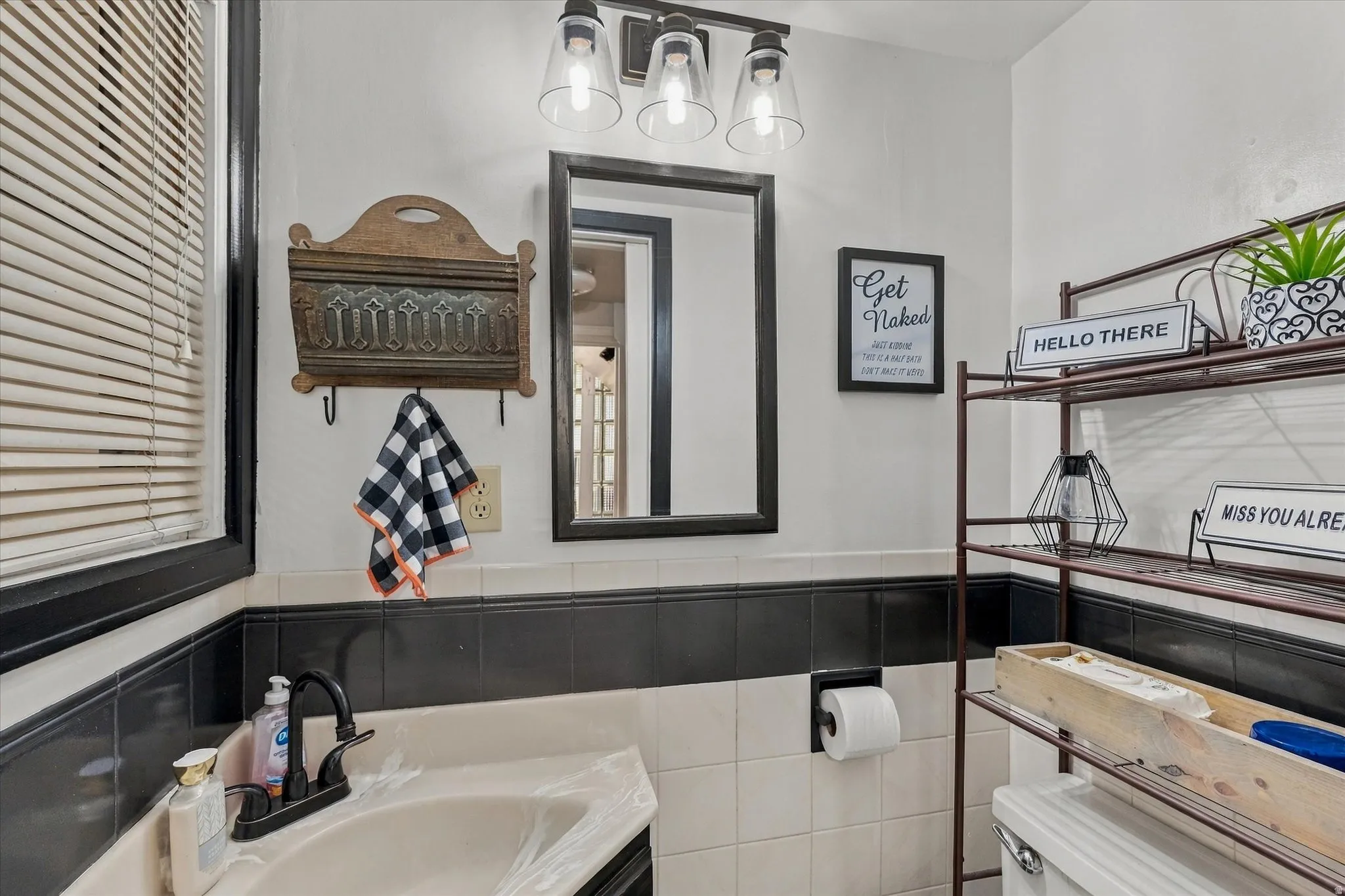 Bathroom with a black and white tiled wainscot, black framed mirror, and a wall-mounted light fixture