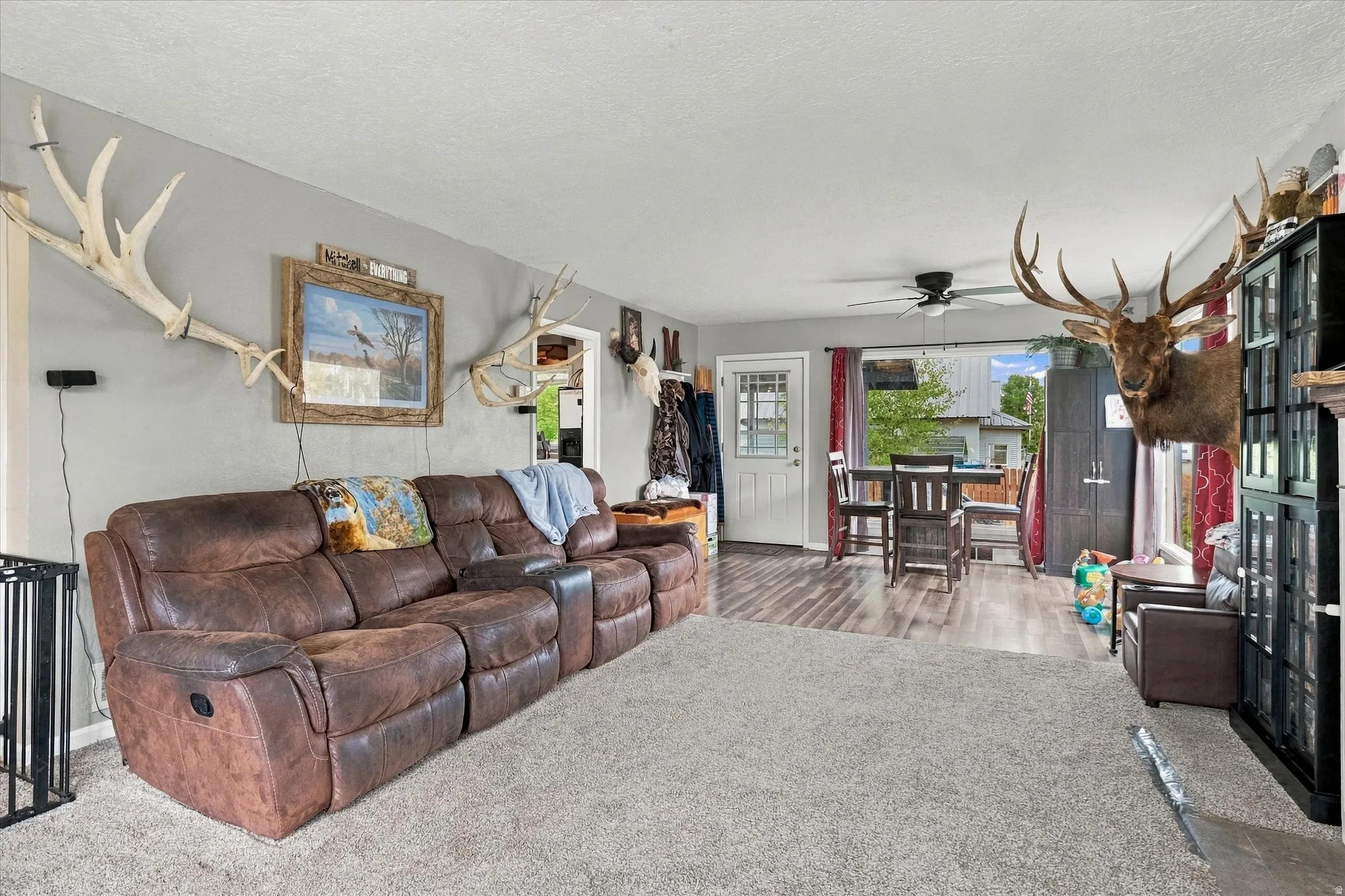 Open-concept living area featuring a light-colored carpet, wood-finish flooring, a ceiling fan, and a dining area with a table and chairs