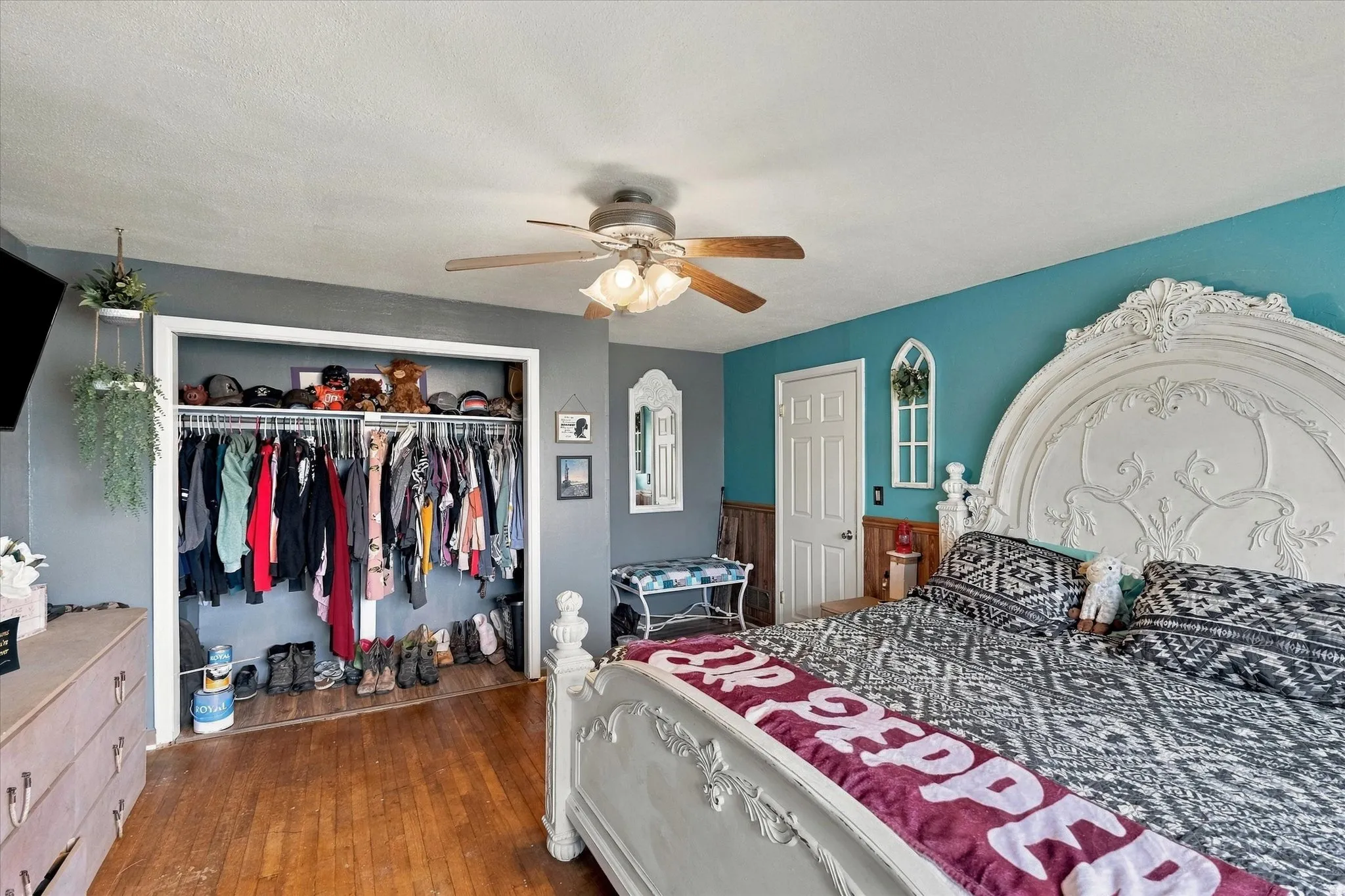 Hardwood flooring, ceiling fan with light fixture, built-in closet with shelving and hanging rod, two-tone wall paint, and white trim