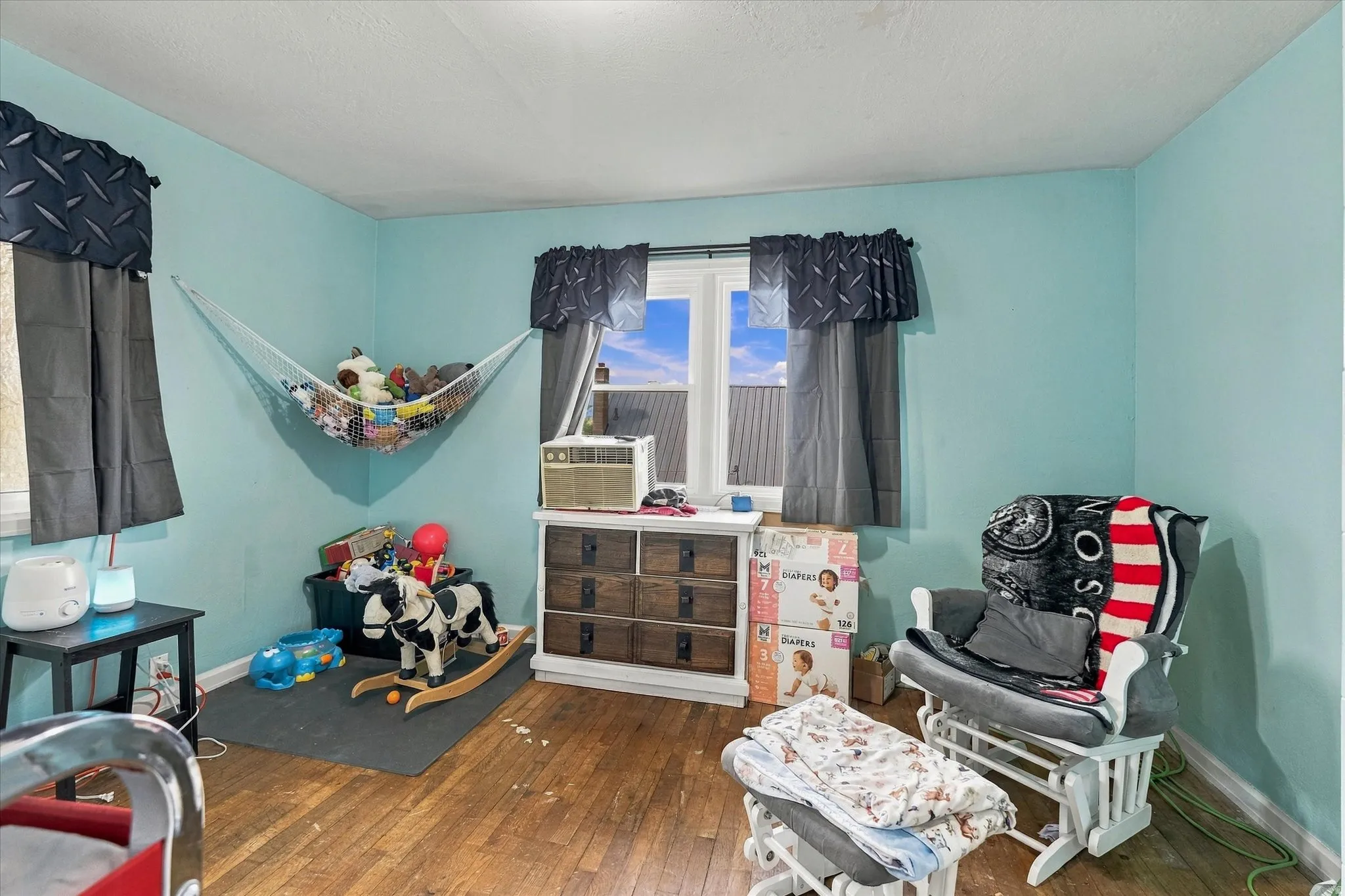 Wood-finish flooring with light blue wall paint, and a window with dark curtains
